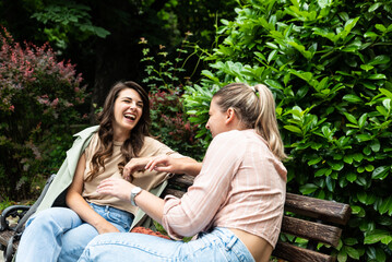 Two best friends talking outside, sitting on a bench in a park. Women friendship on sunny day in the city conversation and happiness.