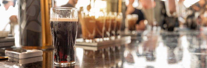 Glasses of stout beer on a bar counter, blurred people, panoramic pub header