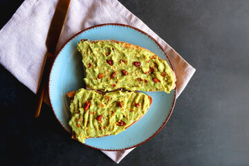 Turquoise plate with two pieces of avocado toast on dark background. Top view.
