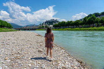 Woman standing in Salzach riverbank in Austria Salzburg with towers and the castle skyline of the...