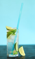 Lemonade with ice and lime on a light blue background. Summer cocktail with a cold drink on a dark table. Refreshing drink with straw close up