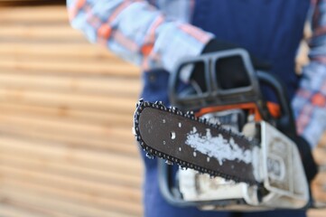 Carpenter with a saw in his hands stands on a background of cut wooden boards.