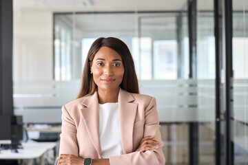 Confident smiling young professional business woman ceo corporate leader, female African American lawyer or leader manager wearing suit standing arms crossed in office, headshot portrait.