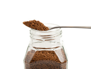 Close-up shot of granulated instant coffee on a spoon over a glass coffee jar.
