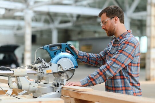 Closeup professional carpenter hold electric circular saw at sawmill. Skilled joiner using circular saw for cutting wood board at woodworking workshop. Furniture production factory. Man cabinet maker