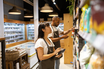 Ethnic sales staff checking tablet for grocery items in shelf