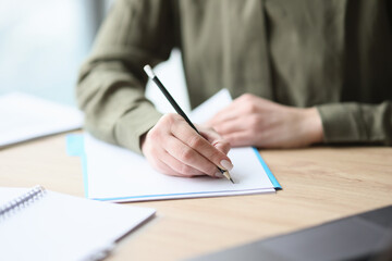 Woman writes on paper sheet with pencil sitting at desk