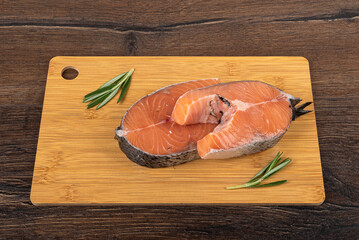 Raw salmon steaks on a wooden cutting board over wooden background.