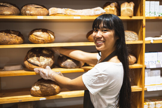 Happy Asian woman with bread loaves in bakery