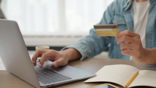male hand holding the credit card and Pressing the Key on the Laptop to make an online payment. E-commerce website payments concept.