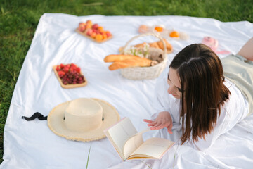 Obraz na płótnie Canvas A beautiful girl meets the summer dawn on the green grass during a picnic.