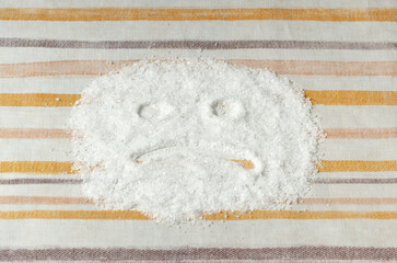 A sad smiley face on a tablecloth as a symbol of the harm of salt to human health.