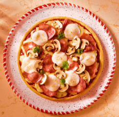 Pizza mit Champignons Mozzarella Pesto und Schinken auf gesprenkeltem Teller mit rot weissem Rand