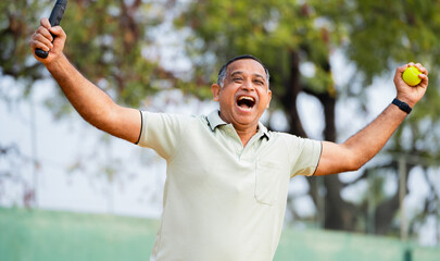 Indian excited senior man celebrating by shouting after winning tennis match at court - concept of...