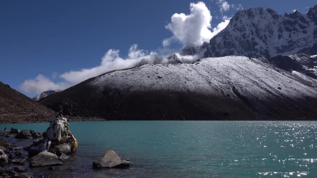 Turquoise Gokyo lake on sunny day, Nepal 
rocky terrain and snow covered peaks with clear blue sky
