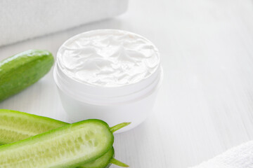 Pure white cucumber moisturizer in a white jar.   White towel. Green Cucumber.