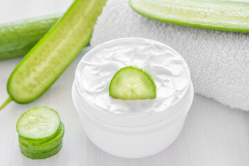 Pure white cucumber moisturizer in a white jar.   White towel. Green Cucumber.