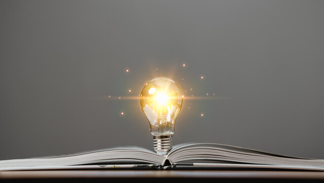 Glowing light bulb with creativity twinkling lights on a book. Ideas for inspiration from reading. Innovation concept of self-learning, education knowledge, technology, business, power of knowledge.