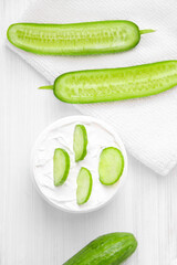 Pure white cucumber moisturizer in a white jar.   White towel. Green Cucumber.