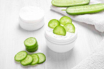 Pure white cucumber moisturizer in a white jar.   White towel. Green Cucumber.