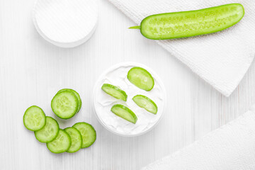 Pure white cucumber moisturizer in a white jar.   White towel. Green Cucumber.