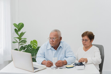 Telemedicine and home health care concept, senior Asian couple Listen to doctor's advice over video call using laptop, in living room at home.