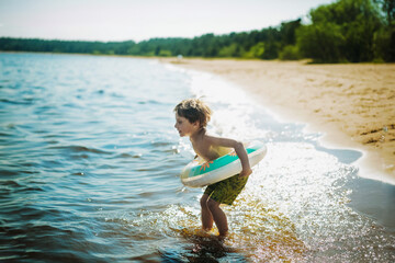 cute caucasian boy running into water with splashes and laughter. Vacation on sea side. Happy childhood. Image with selective focus