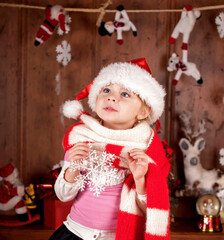 Fototapeta na wymiar A girl in a warm red scarf and a santa claus hat examines paper snowflakes. The child rejoices in winter, New Year cartoons and the holiday of Christmas