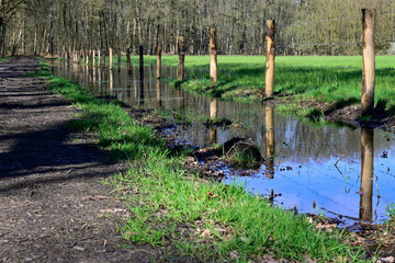 Photograph of a farmland with a large puddle of rainwater after a storm, with a wooden fence