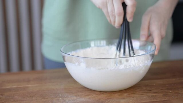 A transparent bowl of dough. The girl stirs with a whisk the dough for the pancakes. Cooking a homemade meal