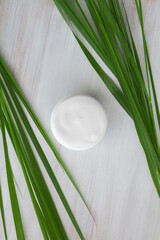 white cosmetic cream on a white wooden background surrounded by long green leaves