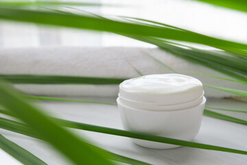 white cosmetic cream on a white wooden background surrounded by long green leaves