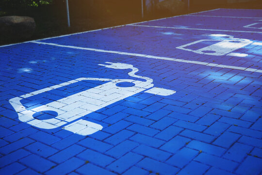 blue painted paved parking lot with charging station for battery electric vehicles. multiple slots with electric car symbol. selective focus. bright warm light mood. modern mobility concept.