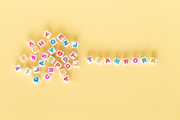 Word Teamwork made out of square beads on pastel yellow background next to pile of random letters