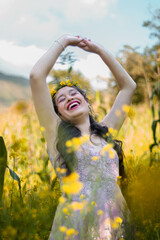 mujer joven en un vestido en campo verde con las manos extendidas al cielo azul y al sol, cabello...