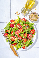 

Summer healthy food, Strawberry arugula salad. Fresh diet fruit strawberry salad with arugula, spinach, lettuce, various nuts and seeds, on white tile background copy space