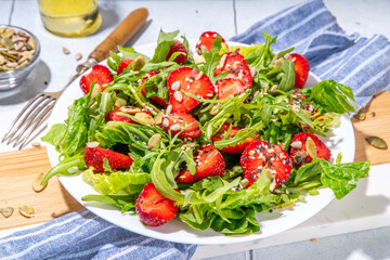 

Summer healthy food, Strawberry arugula salad. Fresh diet fruit strawberry salad with arugula, spinach, lettuce, various nuts and seeds, on white tile background copy space