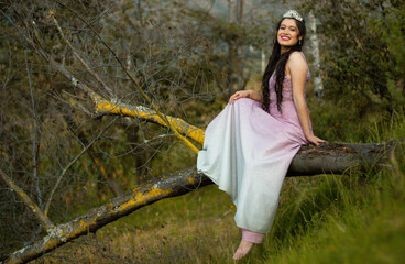 una mujer hermosa con un vestido ligero se sienta en una rama de un  arbol y sobre su cabeza lleva...