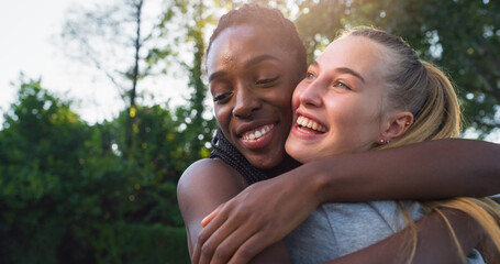 Fototapeta premium Black and Caucasian Girls Happily Meet and Hug at a Basketball Outdoors Court. Female Childhood Friends Reunite and Catch Up After Long Years of Distance. Two Multiethnic Women Talk and Laugh