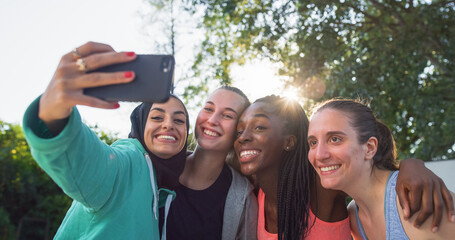 Portrait of Multiethnic Female Friends in Sports Clothes Posing for a Selfie Using a Smartphone. Group of Young Women Celebrating a Win in Outdoor Basketball Court by Taking a Photo for Social Media