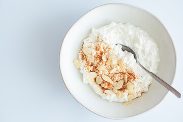 Cottage cheese with cinnamon and almonds in white bowl, white background. Healthy protein breakfast concept.