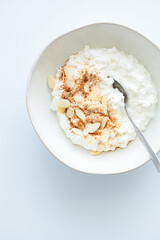 Cottage cheese with cinnamon and almonds in white bowl, white background. Healthy protein breakfast concept.
