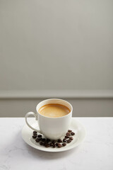 Cup of coffee and beans, on white marble table