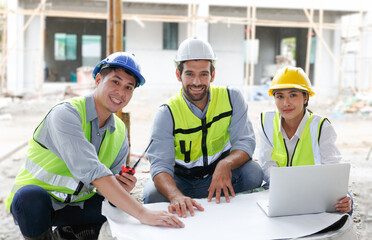 Team of male industrial engineers in helmets discussing new projects while working on blueprints.
