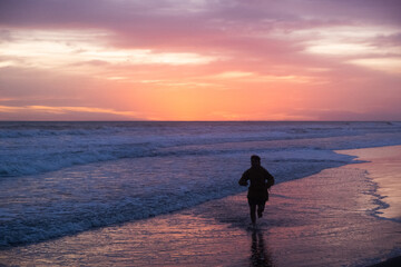 Fototapeta na wymiar Silueta de niño corriendo en la playa durante el atardecer