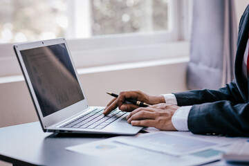 Close up of businessman working at office with laptop, tablet and graph datasheets on his desk