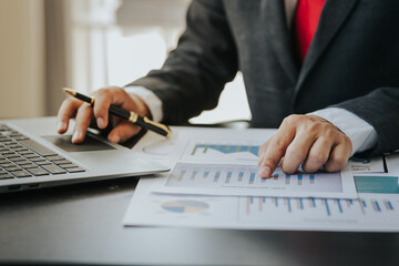 Close up of businessman working at office with laptop, tablet and graph datasheets on his desk