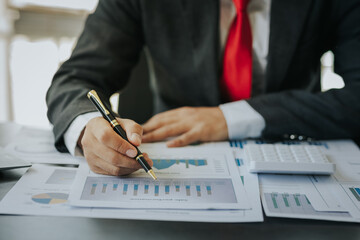 Close up of businessman working at office with laptop, tablet and graph datasheets on his desk