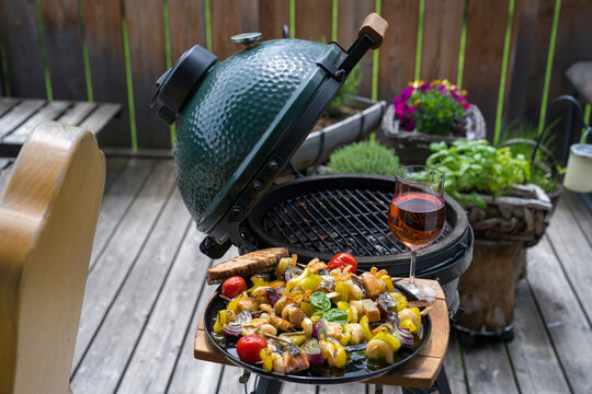 ready to eat - a glas of wine and grilled shrimps with salmon and vegetables on a black plate, from a bbq grill at a summer day on the balcony