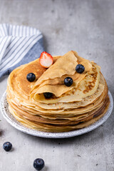 Large stack of traditional thin Russian pancakes on a plate close-up, delicious thin pancakes with berries on a gray concrete table